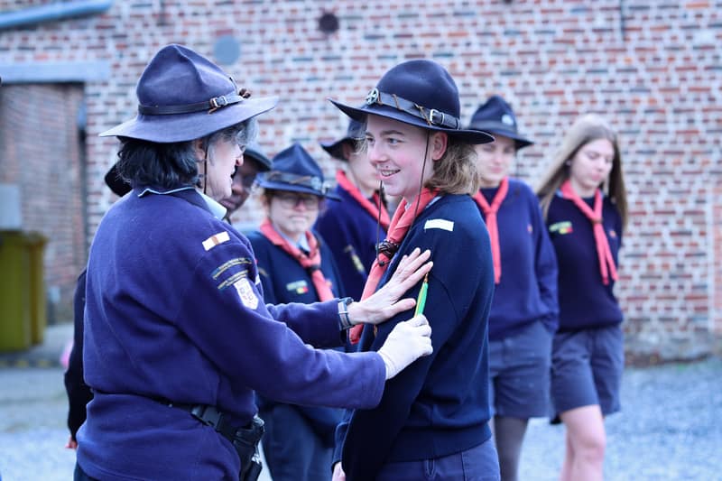Une cheftaine expérimentée aide une plus jeune avec son uniforme lors d'une cérémonie.